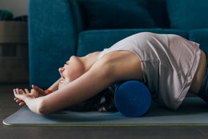 working out at home woman is sportswear using a roller to massage back muscles