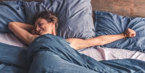 Woman is stretching and smiling while lying in bed in the morning