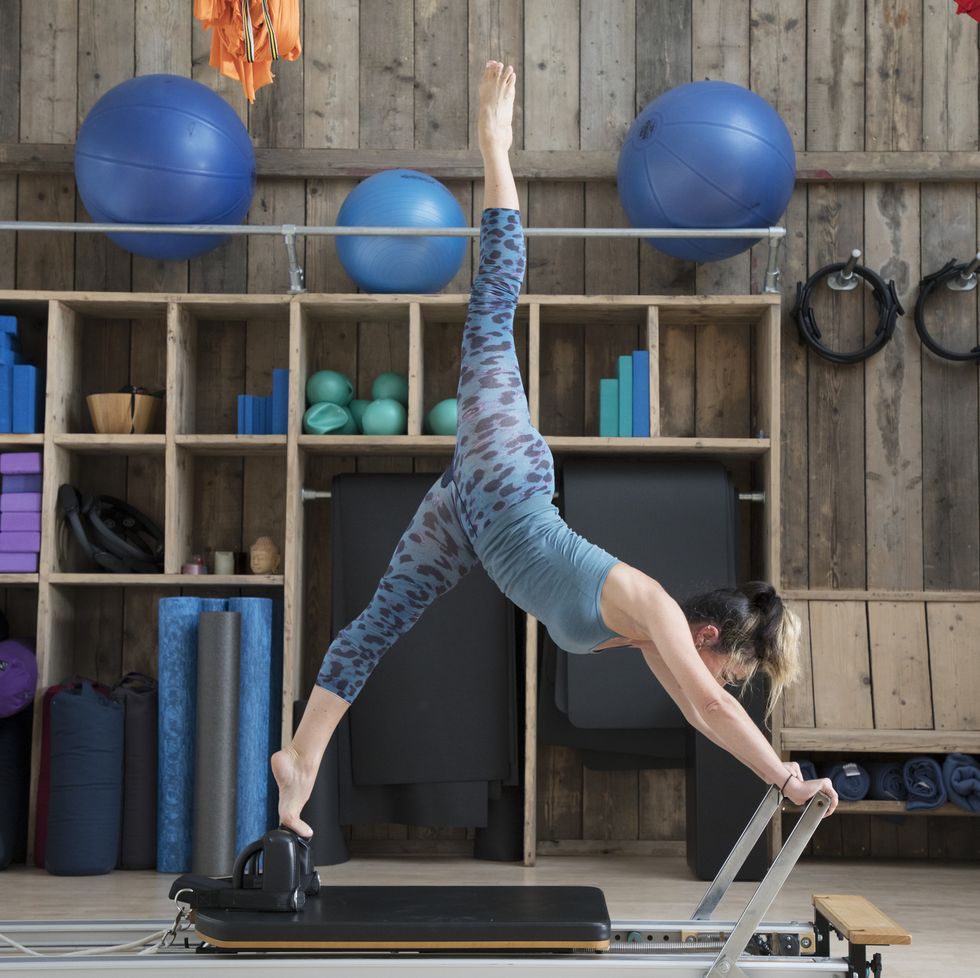 Woman is stretching on a reformer in pilates studio.