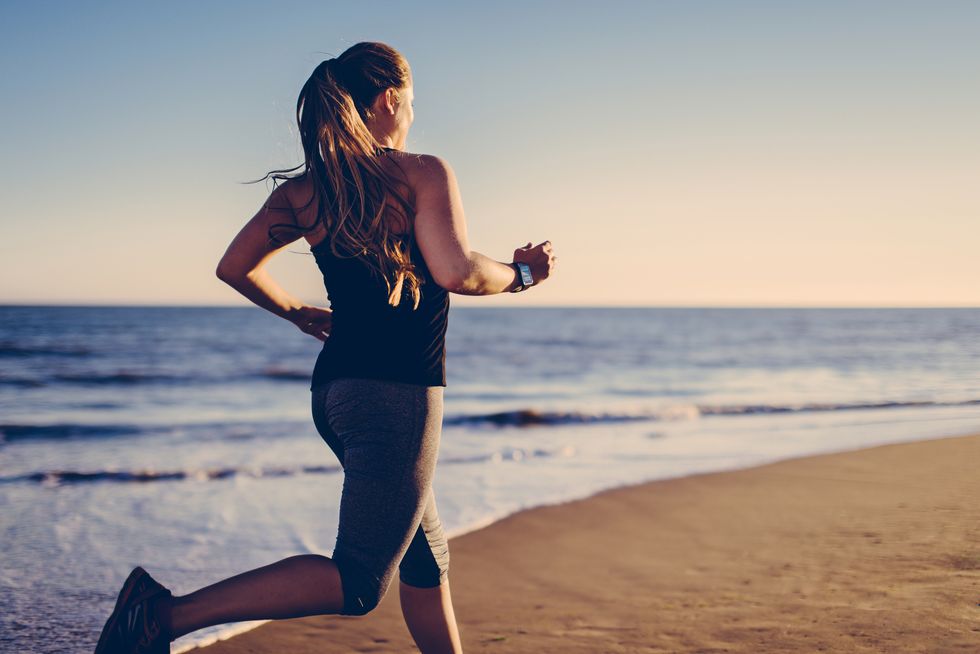 Woman jogging at beach with smartwatch.