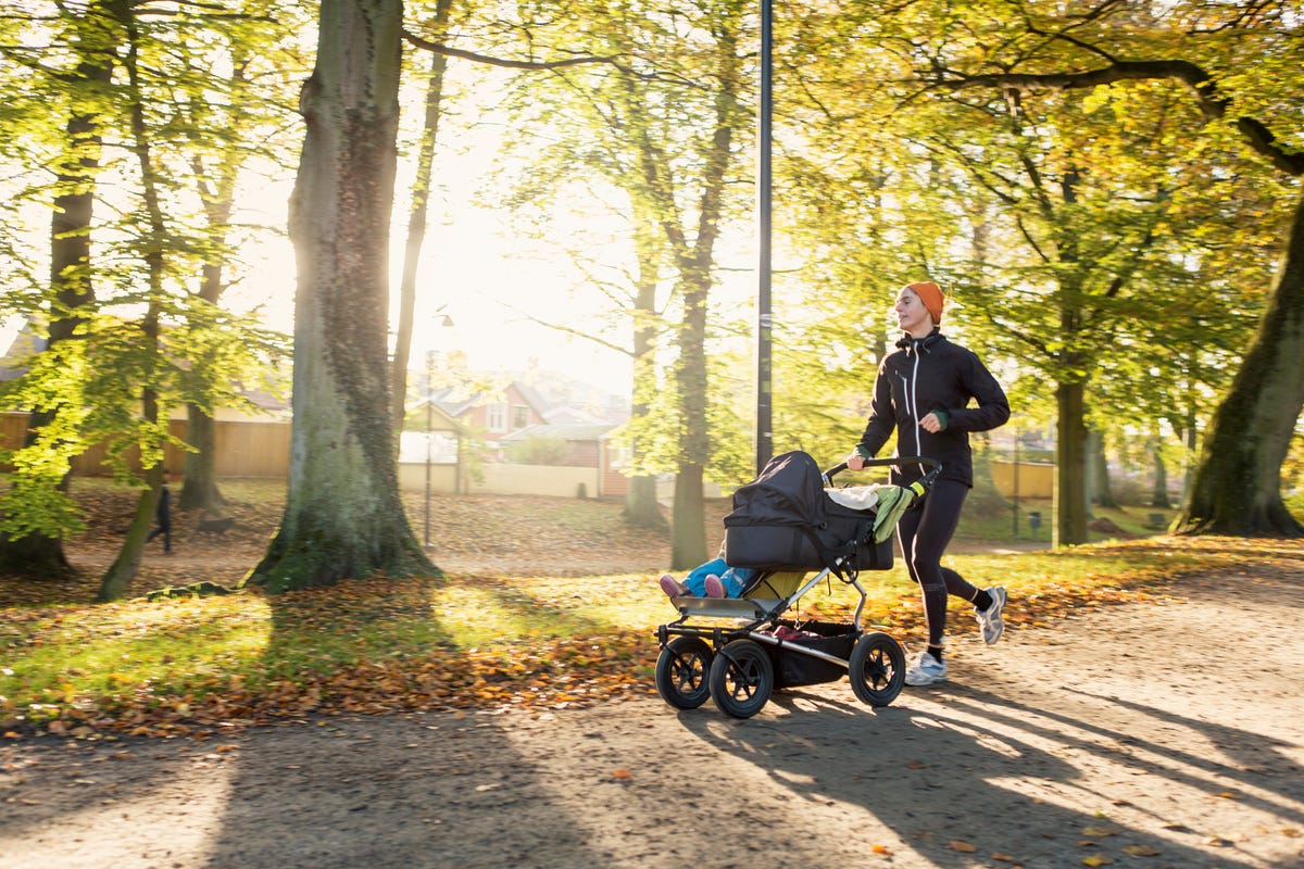 woman jogging with baby stroller on road at park