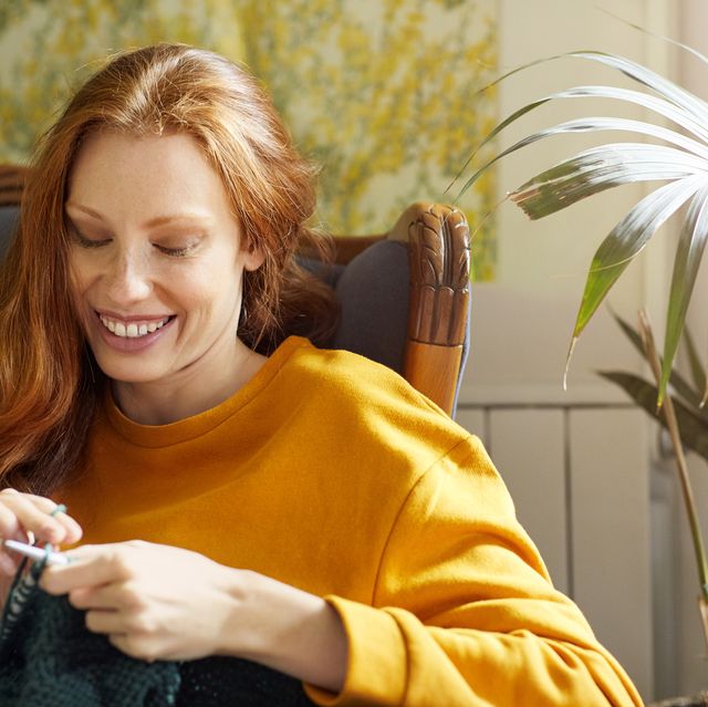 woman knitting while sitting by plant on chair