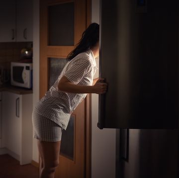 woman leaning into fridge at night searching for food with bad diet habits