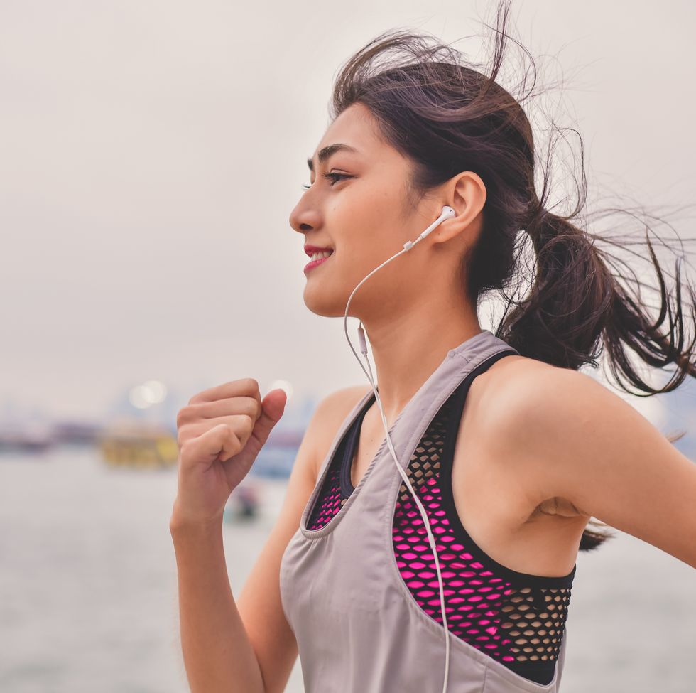 woman listening music while jogging by river against sky