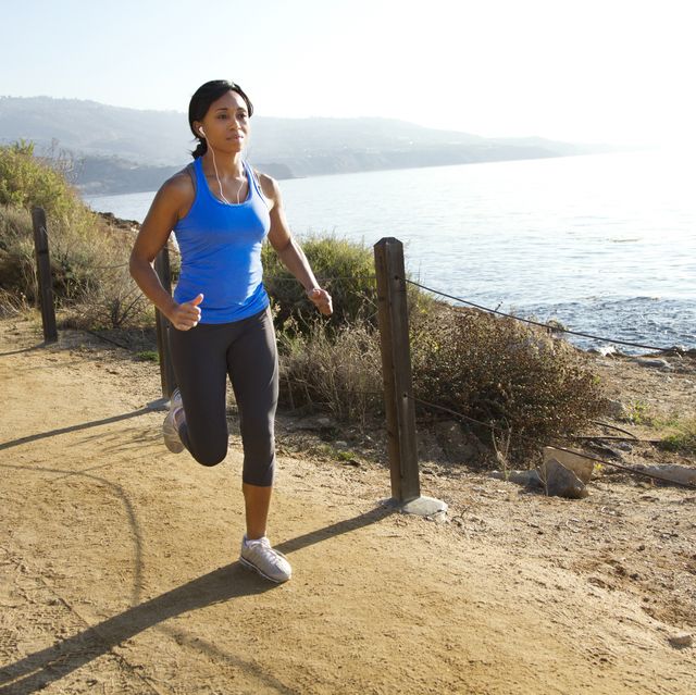 woman listening music while jogging on road against sea