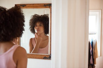 young black woman examining her face in a mirror