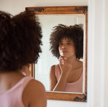 young Black woman examining her face in a mirror young black woman examining her face in a mirror