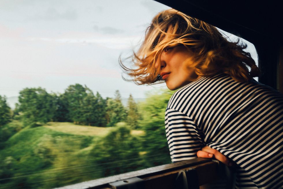 blonde woman in black and white striped shirt with hair blowing in wind looking at the view from train