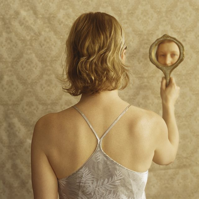 woman looking into hand mirror