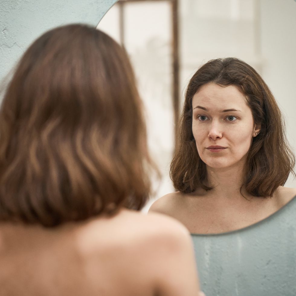 woman looks at her face in the mirror