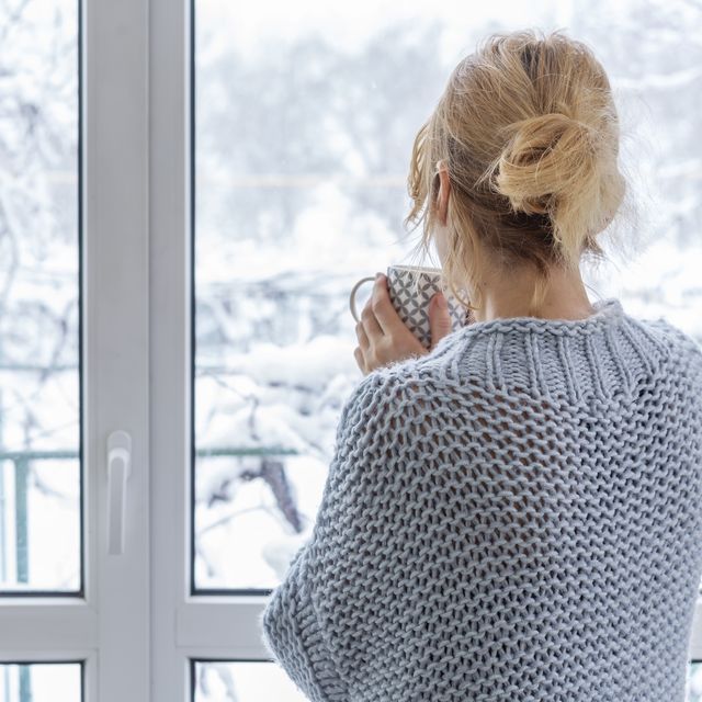 vrouw kijkt uit het raam en buiten ligt sneeuw