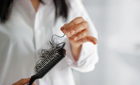 woman losing hair on hairbrush in hand on bathroom background