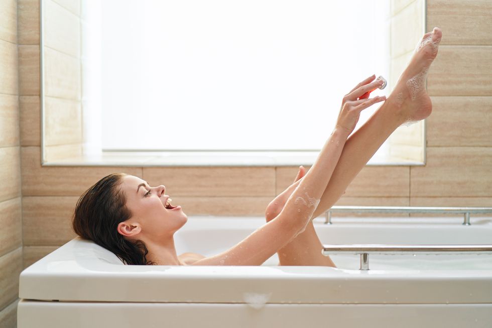Woman lying in a bubble bath and shaves her legs with a razor