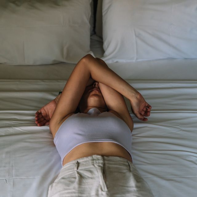 woman lying on a bed covering her face with her arms concept of mental health