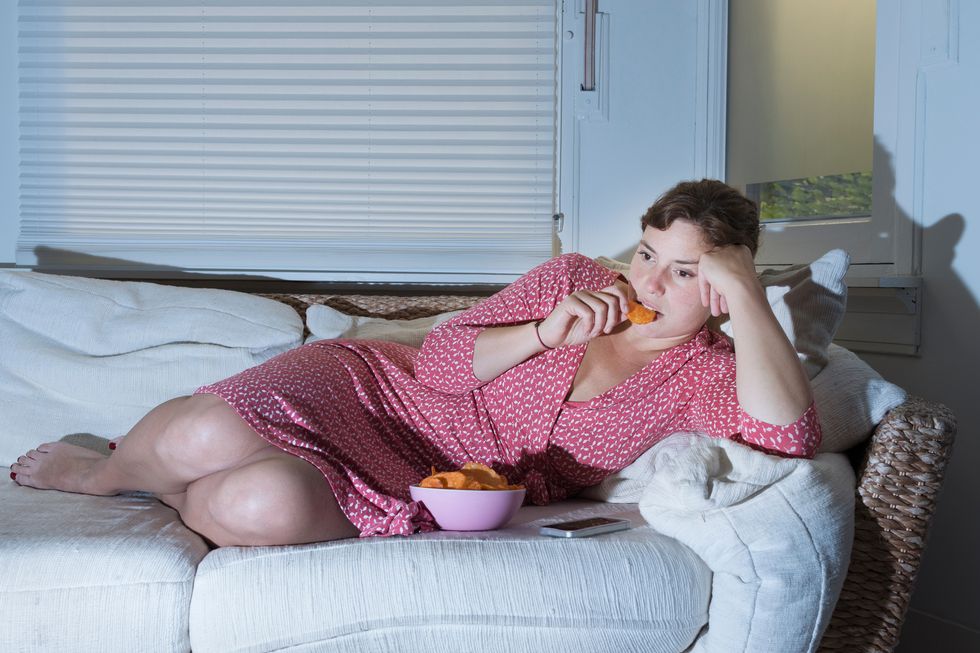 woman lying on sofa eating bowl of crisps