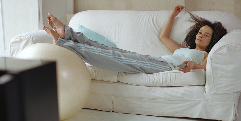 woman lying on sofa using television remote control