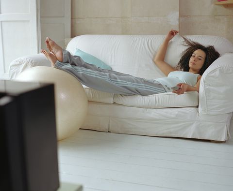 Woman lying on sofa using television remote control