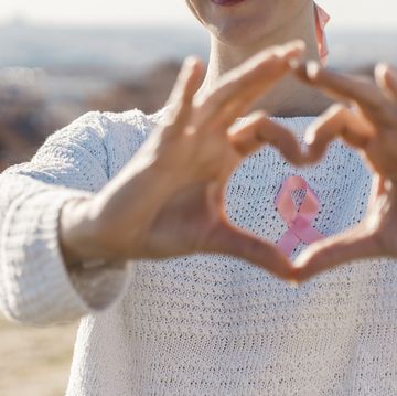 woman making a heart shaped with her hands while using a pink ribbon for support breast cancer cause
