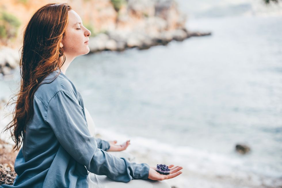 woman meditating and holding crystals against sea
