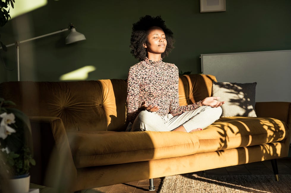 woman meditating while sitting on sofa at home