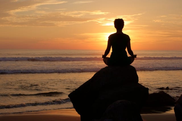 a woman meditation on an ocean side rock