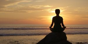 a woman meditation on an ocean side rock