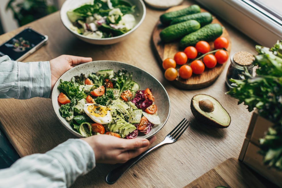 woman mixing delicious superfood salad ingredients with wooden spoons in kitchen