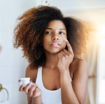 Woman using moisturizer in mirror Woman using moisturizer in mirror