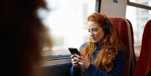 Woman on train listening to music on mobile phone with headphones, London