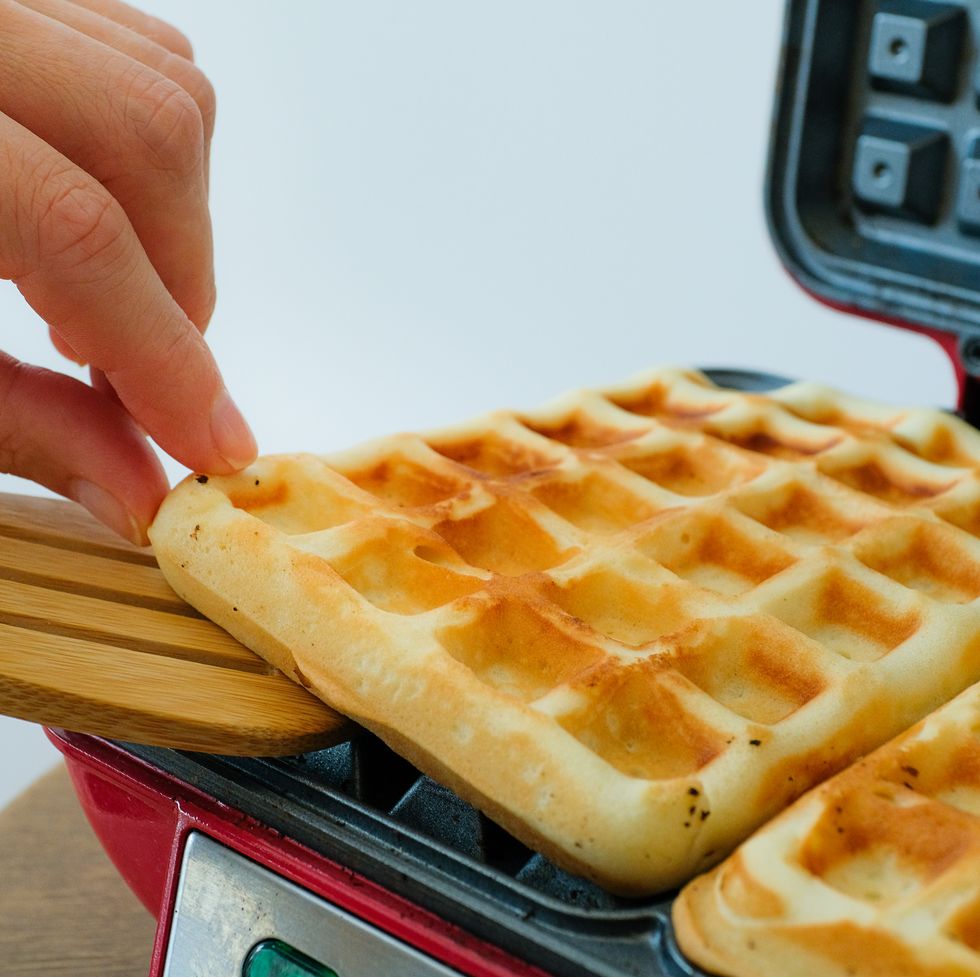 a woman or a girl takes a freshly cooked and baked waffle in a waffle iron to eat it. the concept of cooking homemade food according to a traditional family recipe, hobby, favorite activity. dependence on eating sweets and desserts, overeating.