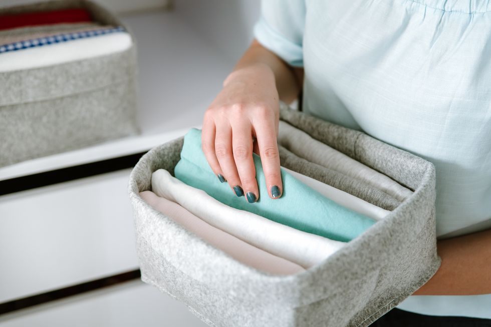 woman organizing clothes in wardrobe, putting shirts in boxes, baskets into shelves. clothes neatly folded after laundry. concept of minimalist lifestyle