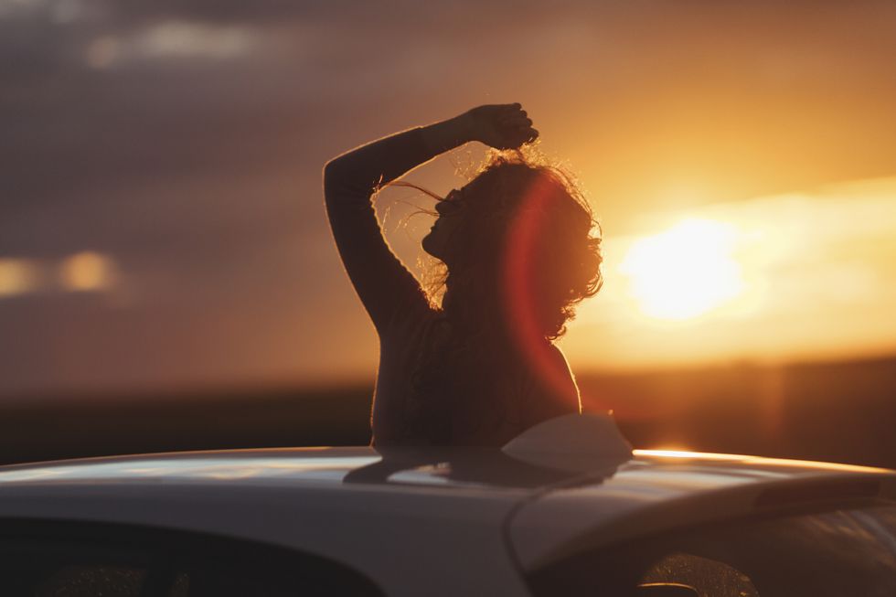 Woman outside the car at sunset, raised arm