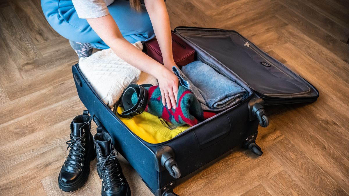 https://hips.hearstapps.com/hmg-prod/images/woman-packing-her-clothes-into-a-suitcase-at-home-royalty-free-image-1703018334.jpg?crop=1xw:0.84415xh;center,top&resize=1200:*