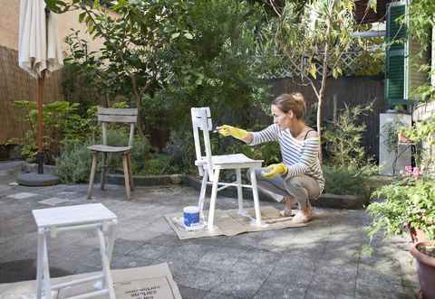 woman painting wooden chairs in garden