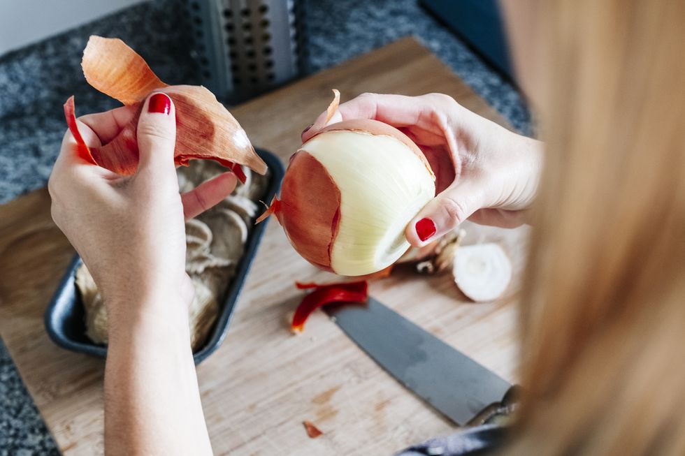 woman peeling an onion with a knife in a kitchen