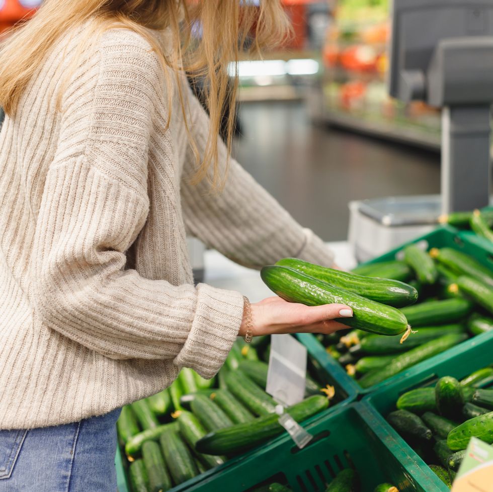 woman pick fresh long cucumbers in shopping trolley at grocery market