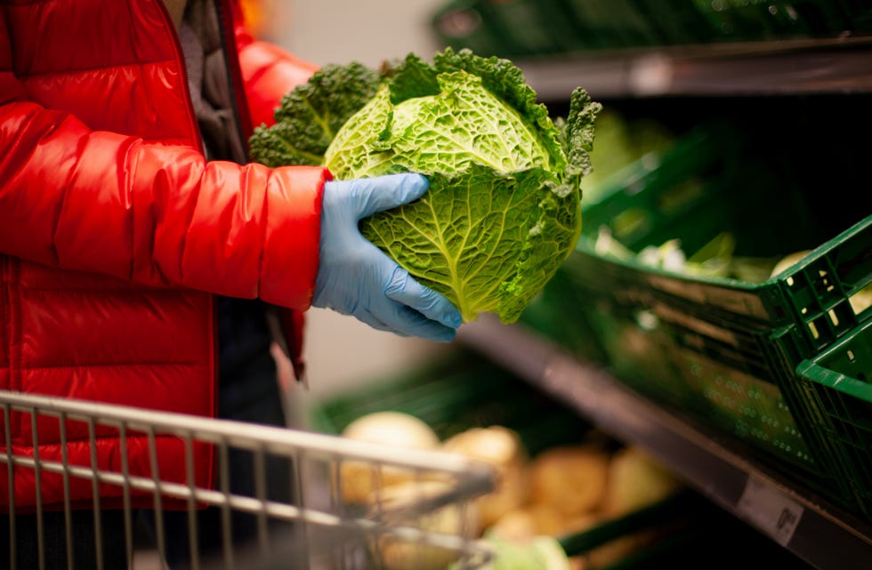 woman picking out savoy cabbage at the supermarket, wearing protective gloves