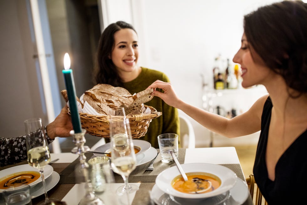 woman picking up bread from basket held by friend during dinner party
