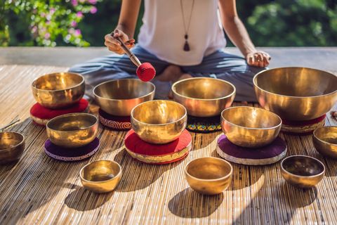 woman playing on tibetan singing bowl while sitting on yoga mat against a waterfall vintage tonned beautiful girl with mala beads meditating