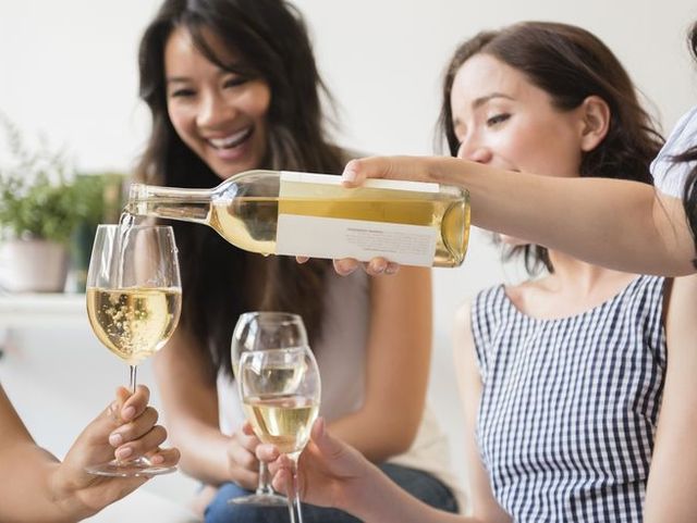 woman pouring bottle of white wine for friends