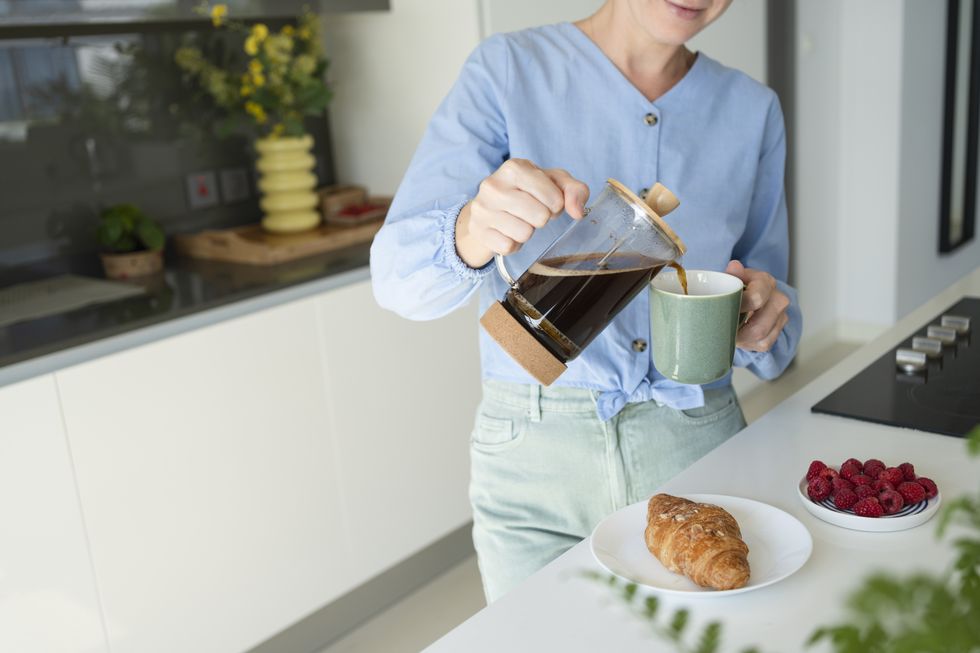 woman pouring coffee in cup with croissant on counter at home