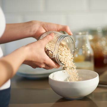 woman pouring oats into bowl in kitchen, close up