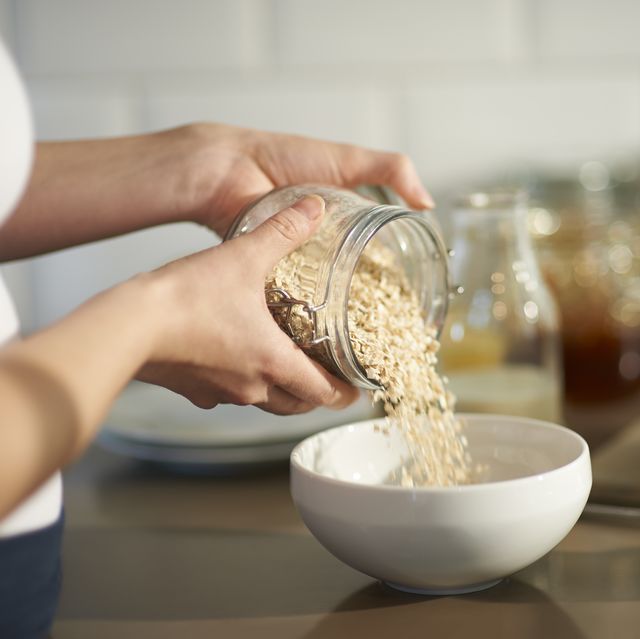 woman pouring oats into bowl in kitchen, close up