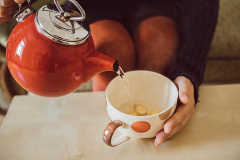 woman pouring water into tea cup with chopped fresh ginger, close up