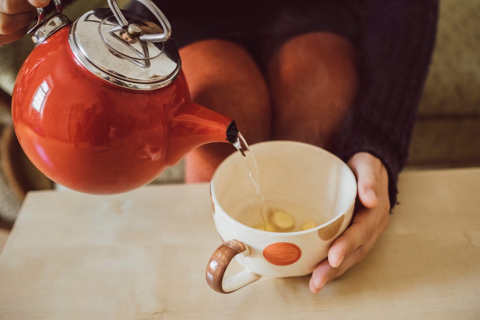 Woman pouring water into tea cup with chopped fresh ginger, close-up