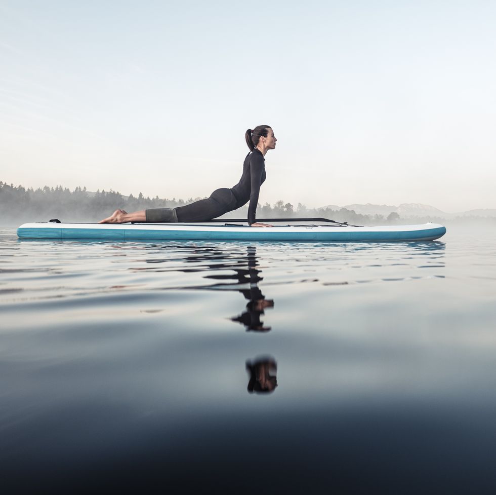 woman practicing paddle board yoga on lake kirchsee in the morning, bad toelz, bavaria, germany