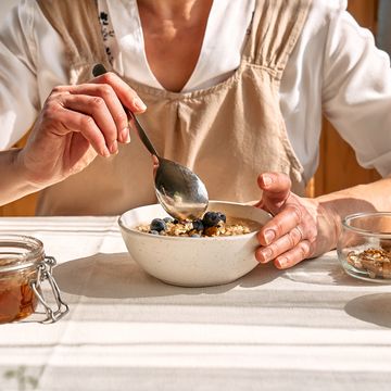 woman preparing healthy dieting vegan nutritious breakfast. female hands holding bowl of oatmeal porridge with blueberries, walnuts and honey.