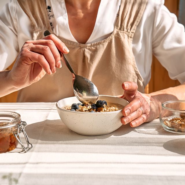 woman preparing healthy dieting vegan nutritious breakfast. female hands holding bowl of oatmeal porridge with blueberries, walnuts and honey.