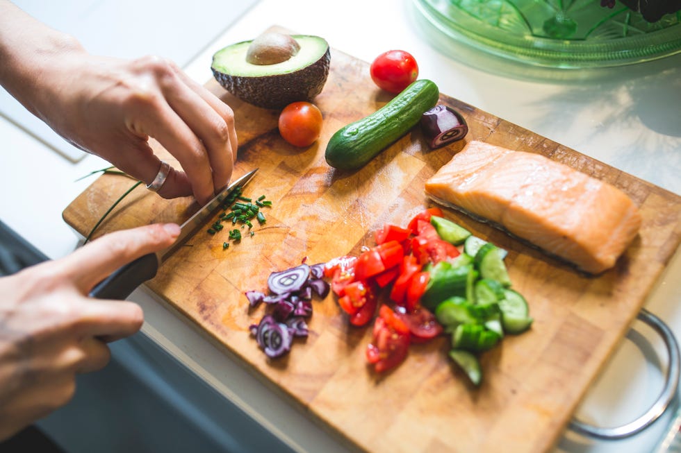 Woman preparing vegetables and salmon on chopping board