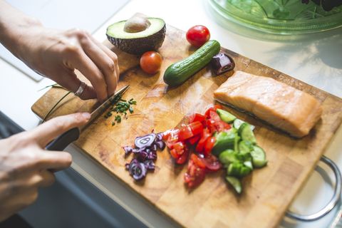 woman preparing vegetables and salmon on chopping board